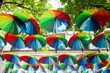 Fototapeta na wymiar Decorative multicolored umbrellas in the center of Paris, Marais. Rainbow and multicolor as symbol of gay, lesbian, bisexual, transgenders. Colorful and beautiful composition. Trees with green leaves