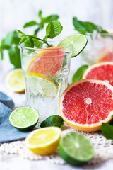 Refreshing healthy alcohol free home made citrus lemonade with pepper mint, limes, lemons, pomelo. Lace napkin, white wooden background. Vacation mood, enjoying summertime, health caring lifestyle