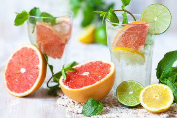 Refreshing healthy alcohol free home made citrus lemonade with pepper mint, limes, lemons, pomelo. Lace napkin, white wooden background. Vacation mood, enjoying summertime, health caring lifestyle