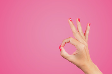 Closeup view of beautiful white female hand isolated on pink background. WOman making ok gesture with rounded fingers. Horizontal color photography.