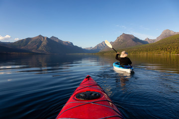 Adventurous Man Kayaking in Lake McDonald during a sunny summer evening with American Rocky Mountains in the background. Taken in Glacier National Park, Montana, USA.
