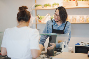 Obraz premium Young Asian owner selling man standing at the counter of a cafe talking to a young woman customer to convince to buy a product in shop. man glad smiling and felling happy.
