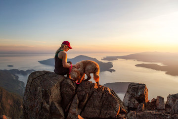 Adventurous Girl is hiking with a dog on top of St. Mark's Mountain during a sunny summer sunset....