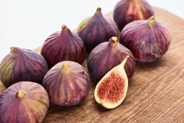 ripe whole and one cut delicious figs on wooden chopping board isolated on white