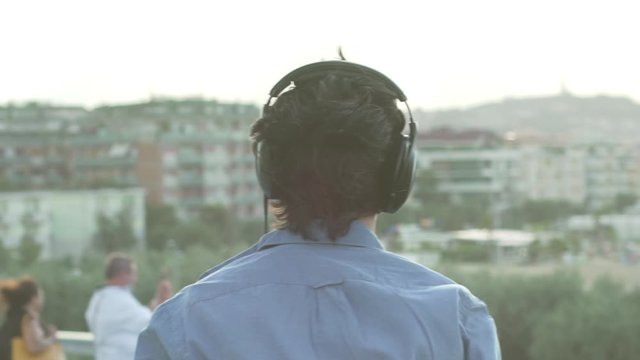 Backshot of young man teenager looking the city with headphones to listen to music in the sunrise or sunset.