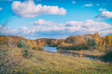 Fototapeta na wymiar Autumn landscape. Blue sky with clouds, small river, orange leaves on trees