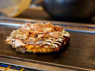 Closeup macro detail of a freshly cooked Okonomiyaki with Katsuobushi, dried fish flakes, sauce, and mayonnaise, on a Teppan grill. Shallow focus. Dotonbori, Osaka, Japan. Travel and cuisine. - 289564491