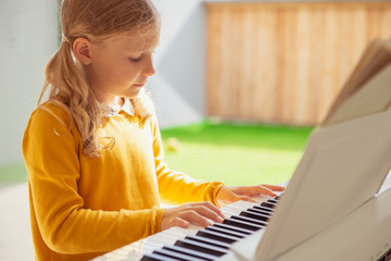 Portrait of pretty little girl having piano lesson at modern white e-piano