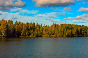 landscape autumn forest by the lake with blue sky and clouds