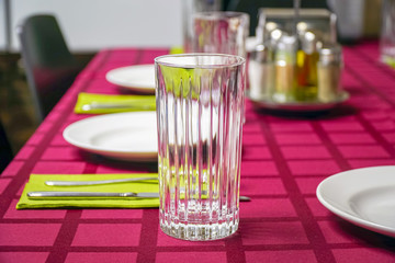 White plate, glass, fork and knife on a napkin. Red tablecloth