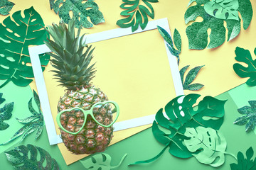 Funny pineapple in sunglasses, frame and paper exotic leaves in neo mint, green and cream yellow