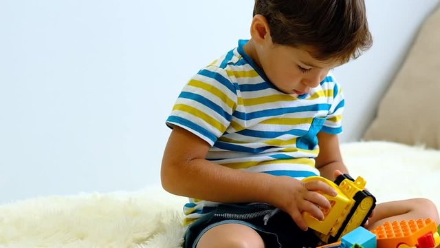 slow motion asian boy playing with colorful construction plastic blocks on white Bed at home .