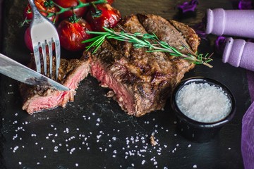 Grilled meat steak on a black board with cherry tomatoes and a sprig of rosemary. Top view, close-up.