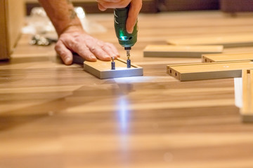 Wooden furniture assembling, woodworker screwing screws using a cordless Assembling furniture from...