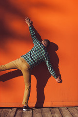 Man in plaid shirt jumping near bright orange wall outdoors