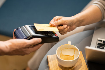 Female hand holding plastic card over electronic payment machine held by waiter