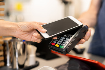 Young woman using her mobile phone for contactless payment while visiting cafe