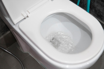 Water flushing in toilet bowl. White hanging toilet seat on white toilet in the home bathroom with grey tiles in concrete style. Bathroom luxury interior.