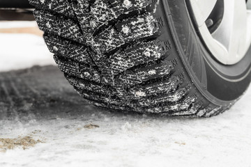 Car wheel on a slippery snowy winter road. Deep tread of winter studded tires close-up.