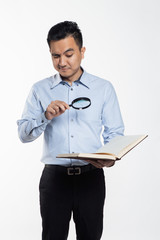 Asian man reading book using a magnifying glass.