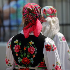 Two women seen on her back, upper parts of body, in colorful traditional folk costumes and head...