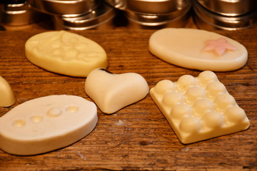 An image of five different decorative soap bars of various shapes of white, light yellow and light pink colors made of natural ingredients lying on a wooden surface 