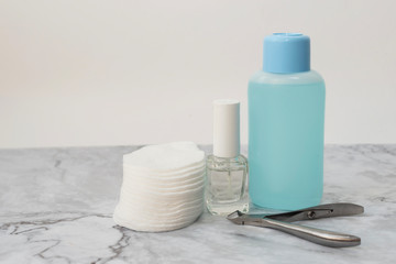 Set of manucure nail care products on a soft marble surface. Glass bottle with colorless firming nail polish, plastic bottle with nail varnish remover and cotton pads. Front view. Copy space for text