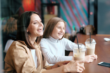 Ecstatic female and her pretty daughter with milk cocktails laughing in cafe