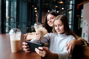 Happy mother embracing her daughter with smartphone while both watching video