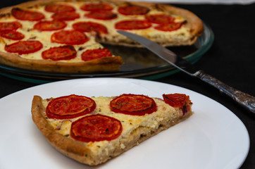 Homemade whole-wheat flour pie with ricotta cheese and tomatoes on a black background. Closeup