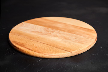 Cutting board on black stone table. Empty round beech wooden chopping board on dark background