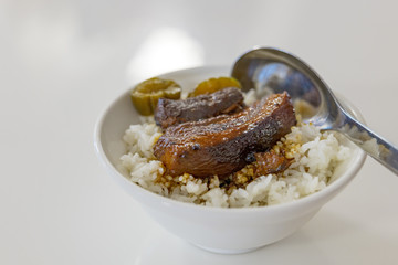 Close up view of Lu Rou Fan, Taiwanese Slow cook Soy Sauce Braised Pork Belly, with rice in small white bowl and white table. 