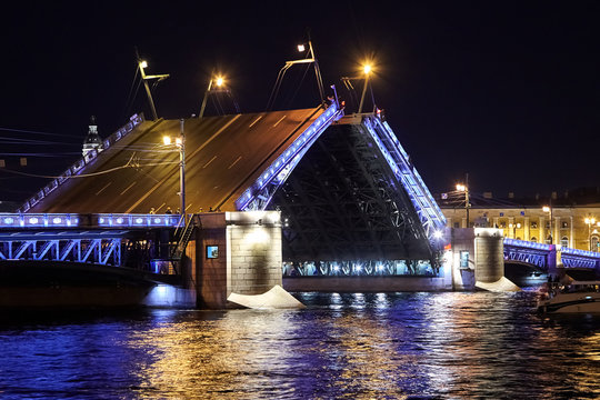 Drawbridge across the Neva River at night. Illuminated Palace Bridge raising. Ripples, colorful reflection of night lights (Saint Petersburg, Russia)