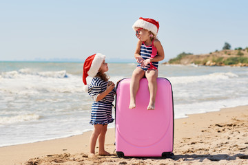 Happy little children girls in Santa hats with suitcase and globe. Kids having fun on summer vacation on Christmas and New year. Holiday Travel and adventure concept