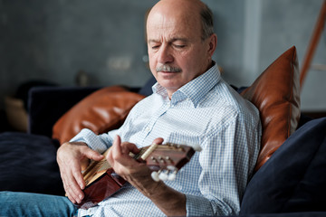 Senior hispanic man at home learning to play guitar. Dad is trying to remember a musical motive.