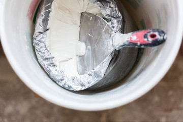 Close-up of spatula in bucket with white putty.