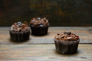 three chocolate cupcakes with cocoa butter cream on dark wood, one is in focus, copy space,