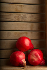 Three large red pomegranates in a wooden fruit box