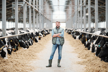 Confident cross-armed staff of farmhouse in workwear standing in long aisle