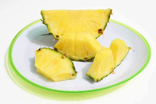 An image of three slices of pineapple and a pineapple quarter on a white plate with a bright green edge on a white background