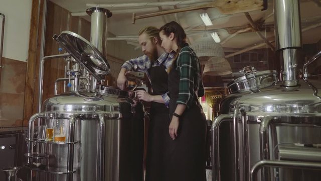 Family business concept. Male and female working with brewing machine at small beer plant.