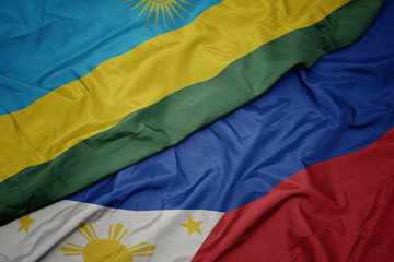 waving colorful flag of philippines and national flag of rwanda.