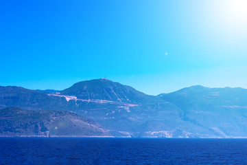 Seascape with mountains, calm blue Meditarrenian sea and bright sunbeams, summer season of tourists, vacation on sunny islands