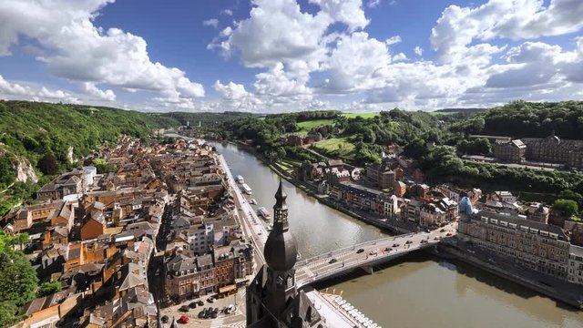 Aerial view from Dinant Citadel, Belgium. Pont Charles de Gaulle bridge and Collegiate Church of Notre Dame de Dinant. Rocky hills and blue sky above River Meuse with architecture offshore. Time lapse