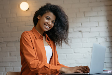 Freelancer typing on keyboard using laptop computer. Portrait of cheerful woman copywriter working...