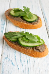 Delicious sandwiches for a snack on the board. Simple healthy food for dinner or breakfast. Slices of white bread with sprat paste, cucumber and parsley. Cold appetizer on a vintage wooden table. 