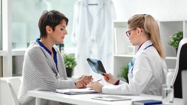 Smiling mature female visiting clinic talking with doctor discussing x-ray image diagnostic
