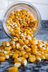 Corn used to make popcorn coming out of a glass pot but uncooked and upopped. Raw ingredient used for food.