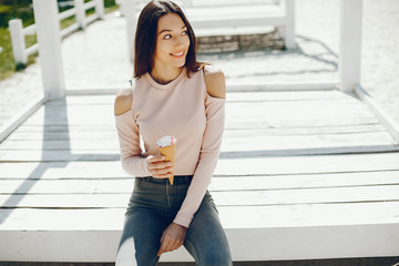 Pretty lady sitting on a summer beach. Cute girl eats the ice cream. Brunette in a pink sweater and gray jeans/