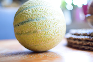 The striped yellow-green melon is located on an old wooden table. Morning sunlight illuminates a ripe melon on the kitchen table.